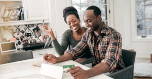Couple smiling while working on a tablet at home.