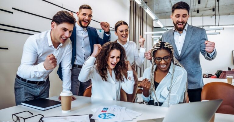 Diverse team celebrates success while gathered around a laptop.