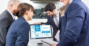 Team of professionals in suits discussing a presentation on a computer screen.