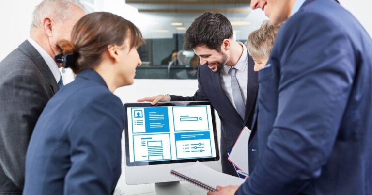 Team of professionals in suits discussing a presentation on a computer screen.