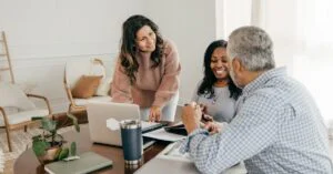 Three colleagues happily collaborating at a table with a laptop and documents.