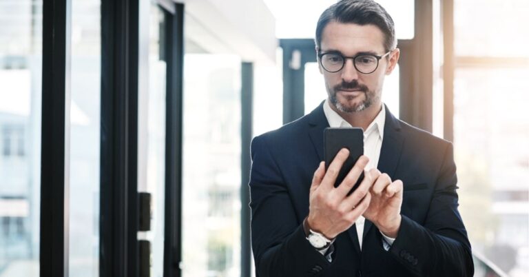 Businessman in a suit using a smartphone in a bright office setting.