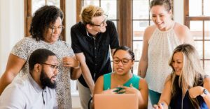 Diverse team gathered around a laptop, discussing and smiling.