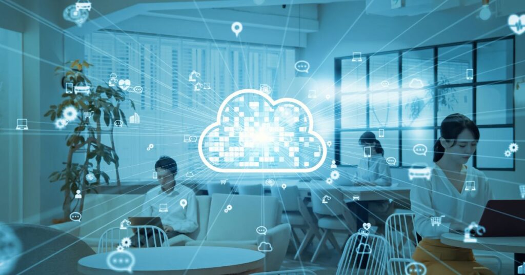 Office workers using laptops in a modern workspace with a digital cloud icon representing data backups in cloud hosting.