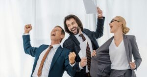 Three colleagues in business attire celebrating together and smiling while holding documents.
