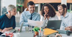 Diverse marketing team collaborating at a modern office table, reviewing a printed report with laptops open