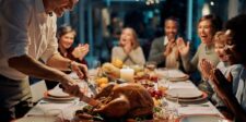 29 Thanksgiving Marketing Ideas to Grow Your Sales Smiling family gathered around a Thanksgiving dinner table while a man carves a roast turkey.