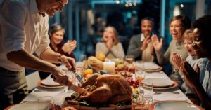 Smiling family gathered around a Thanksgiving dinner table while a man carves a roast turkey.
