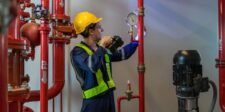 Scaling Safely: Integrating Fire Protection into Your Business Growth Strategy A technician in safety gear is checking a pressure gauge on red fire protection piping next to an industrial pump inside a mechanical room.