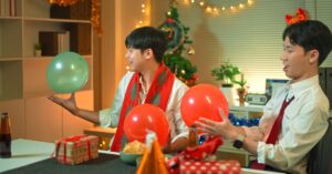 Two coworkers planning Christmas marketing ideas at a holiday-decorated office table with gifts and balloons.