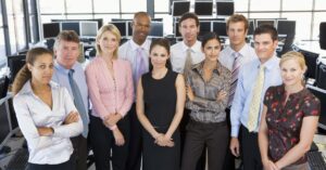 Group of business professionals standing in a modern office with computer monitors in the background.