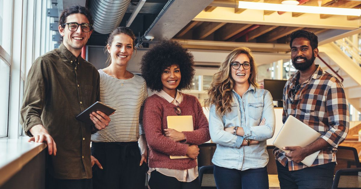 Team photo of five colleagues standing together in a bright, open workspace.
