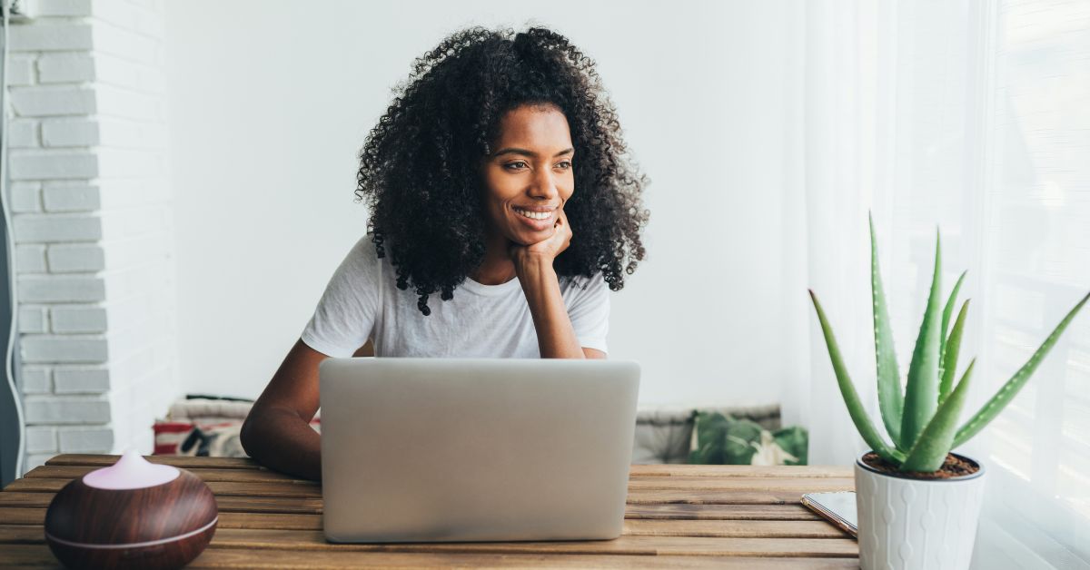 Woman smiling while working on a laptop at a wooden desk