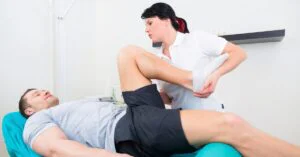 Clinician stretches a patient’s bent leg on an exam table during a physical therapy assessment.
