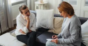 A therapist is taking notes while meeting with a client on a couch during a counselling session.