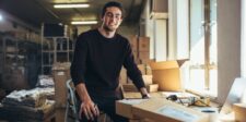 5 Ways Smarter Data Makes Your Small Business Harder to Beat Small business owner in a warehouse workspace surrounded by packages and boxes, smiling while working at a packing table near a laptop.