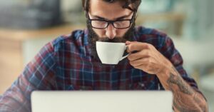 Person working on a laptop while drinking coffee.