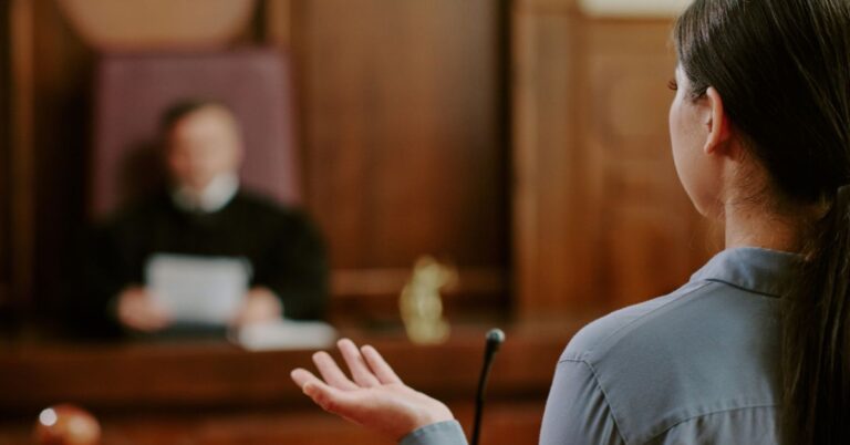 Woman speaking in a courtroom, facing a judge on the bench.