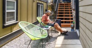 A person working on a laptop on an outdoor patio with a suitcase nearby, illustrating remote work.