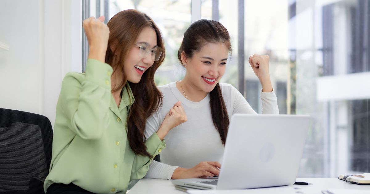 Two people celebrating while reviewing a resume on a laptop in an office.