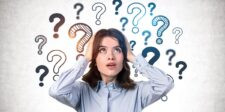 Woman holding her head with multiple question marks floating around her on a light background.