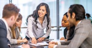 Business team in a meeting as a woman points to a document on the table while others listen.