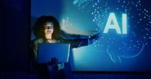 Woman holding a laptop and gesturing toward a glowing AI display on a blue presentation screen with a digital brain graphic in the background.