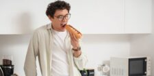 Man in a kitchen about to take a bite of a hot dog