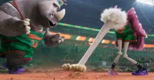 Animated basketball scene showing a rhino and a flamingo in green uniforms facing each other on the court in a packed arena.