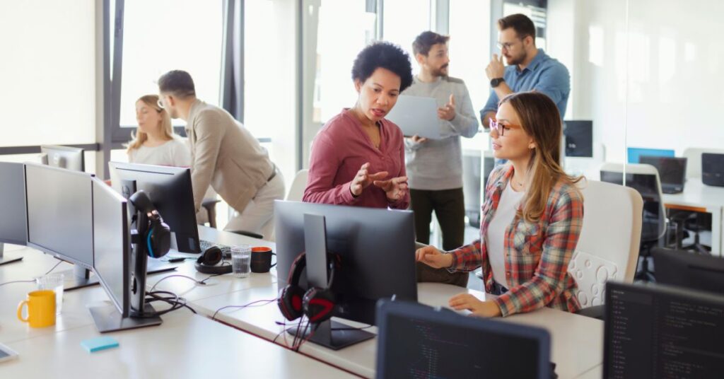 Team of office professionals collaborating around desktop computers in a bright modern workspace.