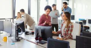 Team of office professionals collaborating around desktop computers in a bright modern workspace.
