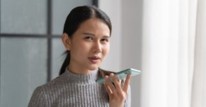 Woman speaking into a smartphone indoors, illustrating how people use AI on their phones today