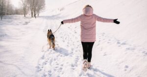 Person in a pink winter jacket walking a dog on a snowy path with visible footprints, symbolizing the traces people leave behind online