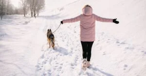 Person in a pink winter jacket walking a dog on a snowy path with visible footprints, symbolizing the traces people leave behind online