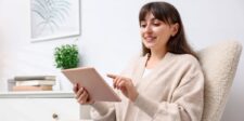 Woman smiling while using a tablet in a bright home office, suggesting someone reading or writing thank you letters online.