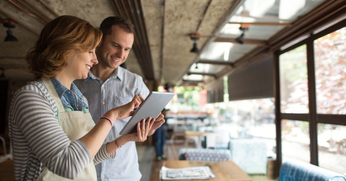 A consultant and small business owner reviewing information together on a tablet inside a café.