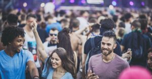 A lively outdoor crowd of young adults smiling and dancing at a music festival, illustrating escapism in marketing.