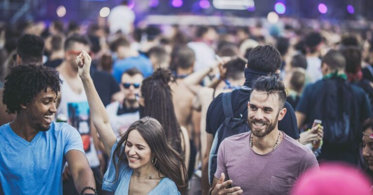 A lively outdoor crowd of young adults smiling and dancing at a music festival, illustrating escapism in marketing.