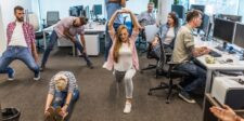 Office workers stretching and moving at their desks during a workplace wellness break.