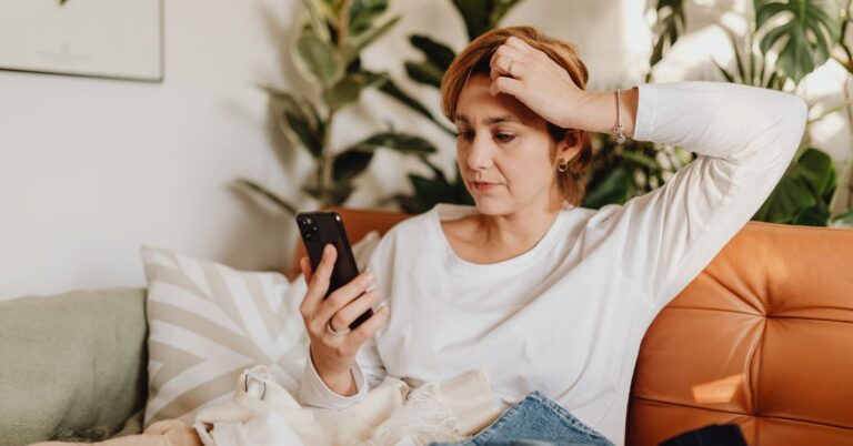 Concerned woman looking at her phone while sitting on a couch, representing confusing or misleading website traffic data