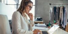 Small business owner working on a laptop in a clothing studio, reviewing information online.