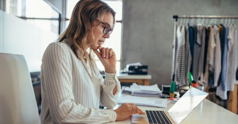 Small business owner working on a laptop in a clothing studio, reviewing information online.