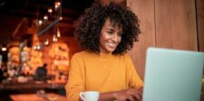 Woman in a yellow sweater smiling while using a laptop in a café