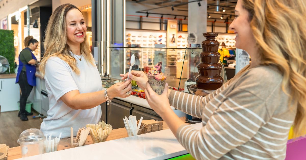 Customer receiving dessert from a smiling small business employee at a dessert shop counter.