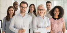 How to Choose a CRM for Businesses: 6 Considerations Group of smiling professionals standing together in a bright office, suggesting teamwork and business collaboration for a CRM-related article.