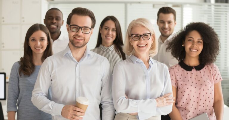 Group of smiling professionals standing together in a bright office, suggesting teamwork and business collaboration for a CRM-related article.