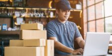 Ecommerce worker using a laptop beside stacked shipping boxes, representing Shopify AI content and online store operations