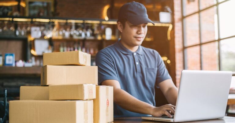Ecommerce worker using a laptop beside stacked shipping boxes, representing Shopify AI content and online store operations