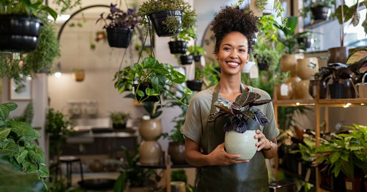 Smiling small business owner holding a potted plant inside a flower shop, representing local business growth and online support.