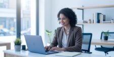 Business owner working on a laptop in a bright office while reviewing online information.